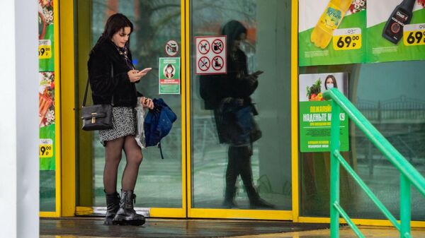 Девушка со смартфоном возле дверей торгового центра