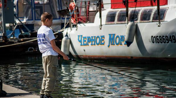 Мальчик ловит рыбу на набережной в Балаклаве