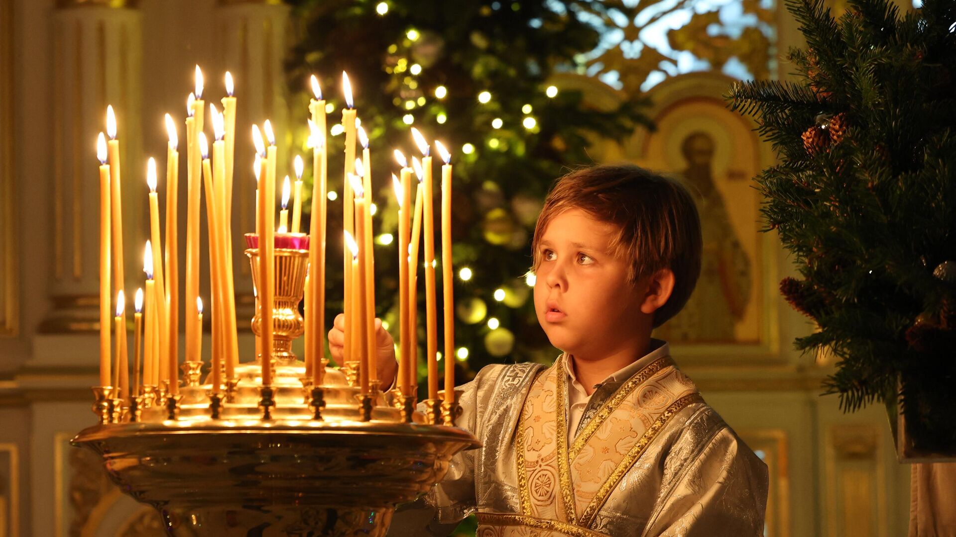 Мальчик зажигает свечу во время празднования православного Рождества в Русской православной церкви в Шардже - РИА Новости, 1920, 07.01.2023