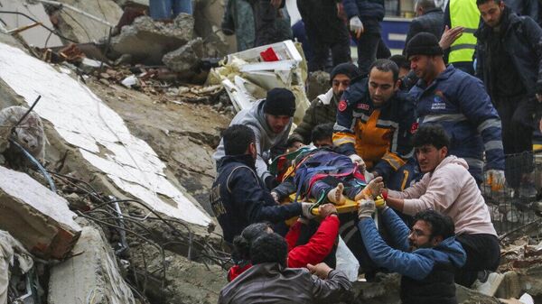 Люди и бригады скорой помощи спасают человека на носилках из рухнувшего здания в Адане, Турция