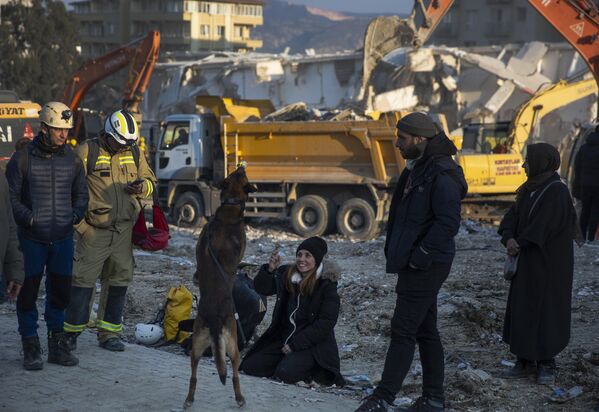 Женщина играет с собакой, пока спасатели продолжают поиски жертв землетрясения в Антакье, Турция