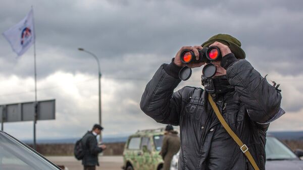 Местный житель наблюдает в бинколь за военным блокпостом на въезде в аэропорт Бельбек рядом с Севастополем