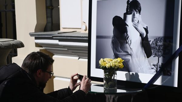 Мужчина фотографирует цветы и портрет модельера возле дверей в Дом моды Валентина Юдашкина
