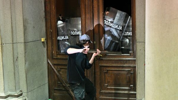 Протестующий использует металлический предмет против полицейских, охраняющих вход в здание городского совета Белграда, во время демонстрации в Белграде