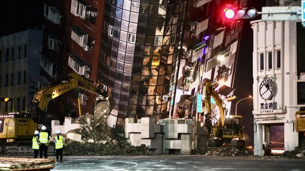Сотрудники службы экстренной помощи стоят перед частично разрушенным зданием, склонившимся над улицей в Хуаляне, 3 апреля 2024 года, после сильного землетрясения, произошедшего на востоке Тайваня