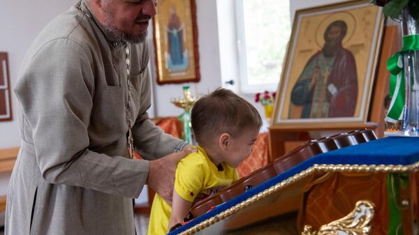 Отец Олег прикладывает своего сына к иконе в храме Вячеслава Чешского в селе Охотское, где он служит.