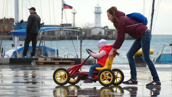 Женщина катает ребенка в детской машине на набережной Ялты
