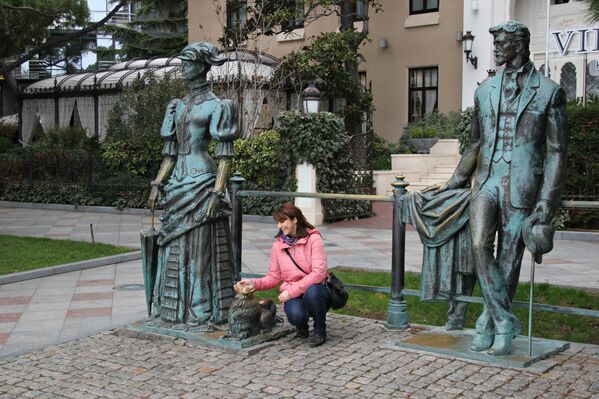 Женщина фотографируется с памятником Дама с собачкой на набережной Ялты