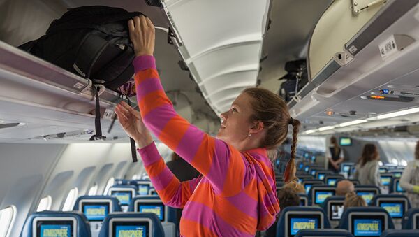 Девушка убирает ручную кладь в отсек в салоне самолета