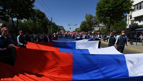 Участники Первомайского шествия несут большой флаг России