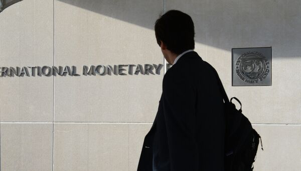 Мужчина у здания Международного валютного фонда смотрит на логотип МВФ на стене.