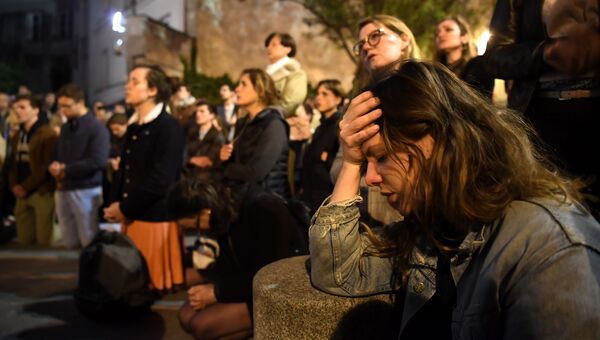 Люди становятся на колени на тротуаре, молясь о спасении собора Нотр-Дам в Париже