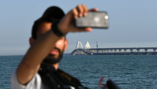Мужчина делает селфи на фоне Крымского моста