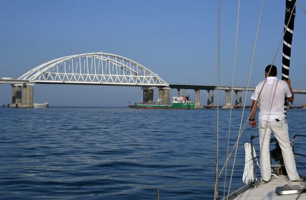 Мужчина смотрит на корабль, который проходит под арками Крымского моста
