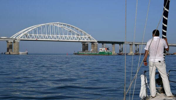 Мужчина смотрит на корабль, который проходит под арками Крымского моста