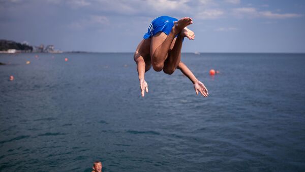 Отдыхающие прыгают с пирса на пляже в Ялте