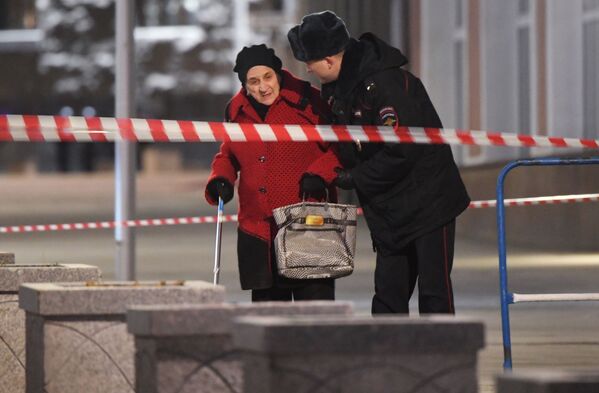 Сотрудник полиции помогает женщине пройти в зоне оцепления недалеко от здания ФСБ на Лубянской площади в Москве, где произошла стрельба