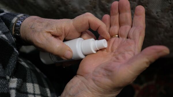 Пожилой мужчина обрабатывает руки антисептиком у себя дома во время самоизоляции. Архивное фото