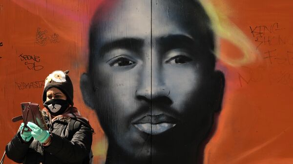 Женщина в маске фотографирует себя на фоне граффити с лицом рэпера Тупака Шакура 5 мая 2020 года в районе Гарлема в Нью-Йорке.