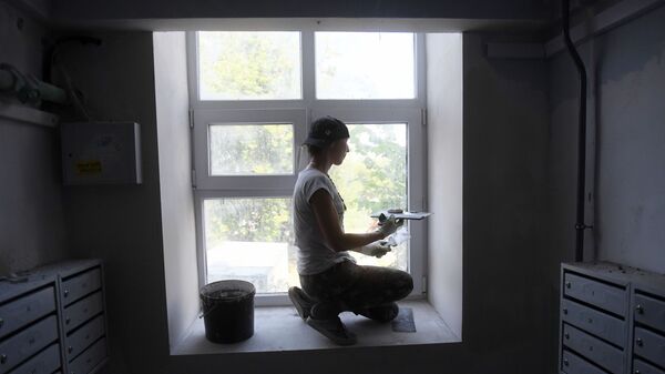 Маляр шпаклюет окно во время капитального ремонта в подъезде жилого дома 