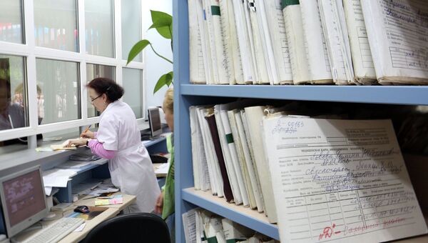 Медицинский работник выдает медицинскую карту пациенту в регистратуре районной поликлиники