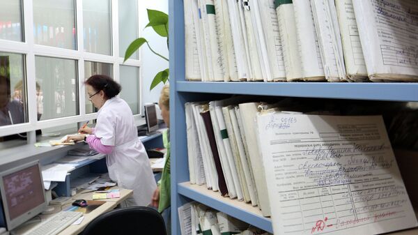 Медицинский работник выдает медицинскую карту пациенту в регистратуре районной поликлиники